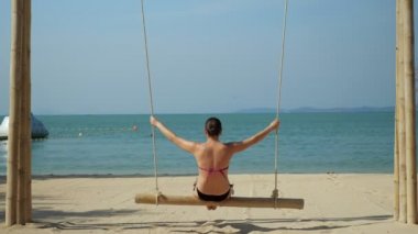 Kadınlar okyanus kıyısındaki egzotik tatil beldesinde salıncakta sallanıyor