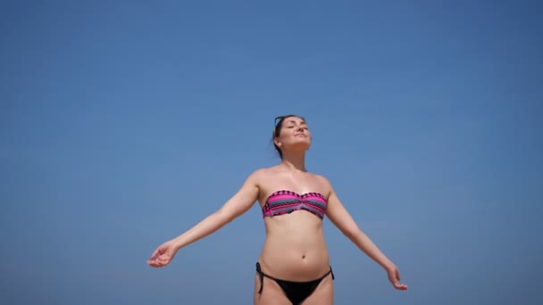 Ontspannen vrouw staat op het strand zonnebaden tegen de hemel — Stockvideo
