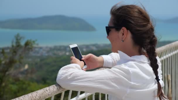 Jovem mulher tipos no telefone inclinando-se no ponto de vista corrimãos — Vídeo de Stock