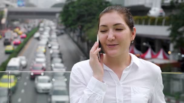 Νεαρή γυναίκα μιλάει σε λευκό smartphone και χαμογελά χαρούμενα — Αρχείο Βίντεο