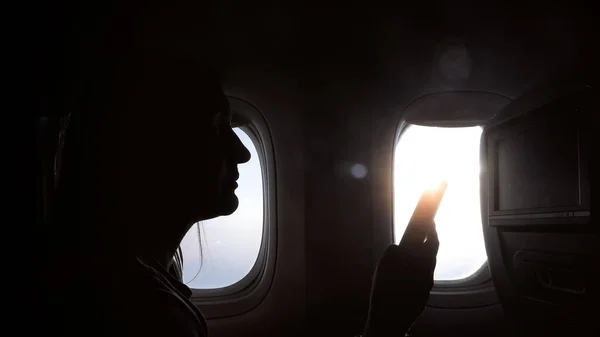 Sylwetka dziewczyny siedzi ze smartfonem przed oknem w samolocie — Zdjęcie stockowe