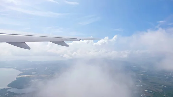 Skrzydło samolotu przelatującego przez chmury nad cofającym się lądem — Zdjęcie stockowe