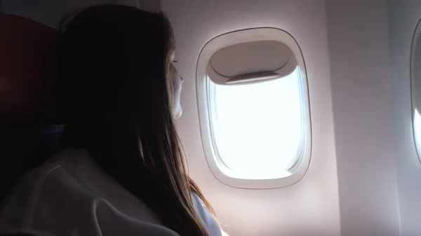 Kobieta z brązowymi włosami wygląda przez otwór w samolocie zbliżenie — Zdjęcie stockowe