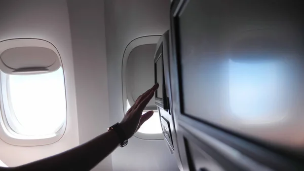 woman hand touches seatback screen in airplane closeup