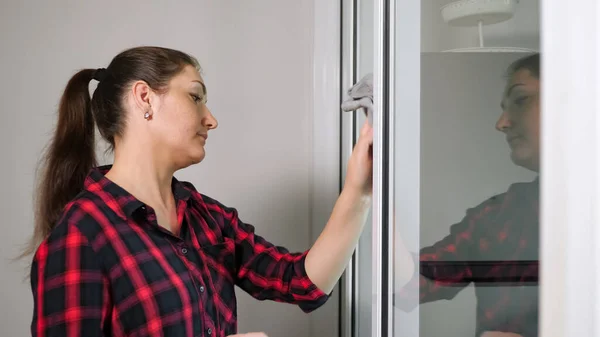 Pretty girl wipes transparent door with grey rag — Stock Photo, Image