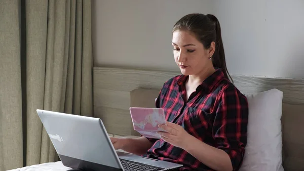 Senhora com rabo de cavalo olha para o passaporte e tipos no laptop — Fotografia de Stock