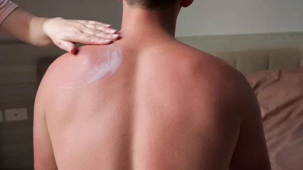 Young woman hand covers muscular man back with white cream — Stock Photo, Image