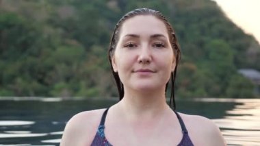 Güzel kız gülümser ve yüzme havuzundaki kameraya bakar.