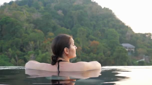 Brunette se retourne avec sourire dans une grande piscine extérieure — Video