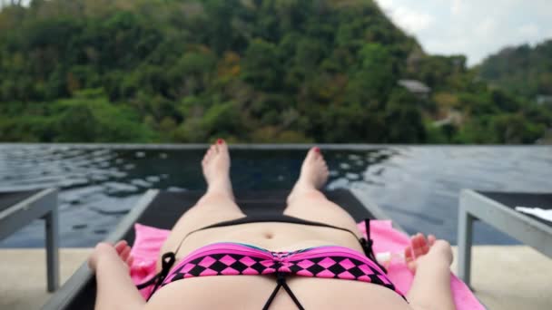 Dame im schwarz-lila Bikini liegt auf Hotelpool-Liege — Stockvideo