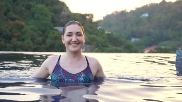 Lächelnde Dame im farbigen Badeanzug nähert sich im blauen Pool — Stockvideo