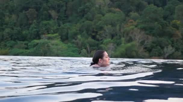 Brunette swims in hotel outdoor swimming pool against plants — Stock Video