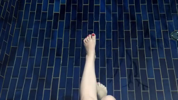 Femme balançant jambes nues avec manucure rouge dans l'eau de piscine — Video