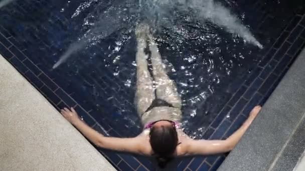 Lady in bikini lies in large swimming pool jacuzzi corner — Stock Video