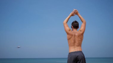 Kumsaldaki genç sporcu ellerini uçağa doğru sallıyor. Arkadan bak.