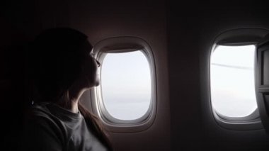 Gri tişörtlü kadın silueti uçağın parlak camlarına karşı