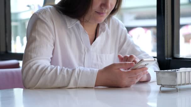 Kvinna i vit skjorta med en telefon vid ett bord på ett café — Stockvideo