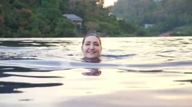 Renkli mayo giymiş gülümseyen kadın mavi havuzda yaklaşıyor.