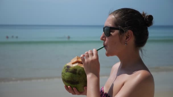 Egy nő a parton kókuszt iszik. — Stock videók