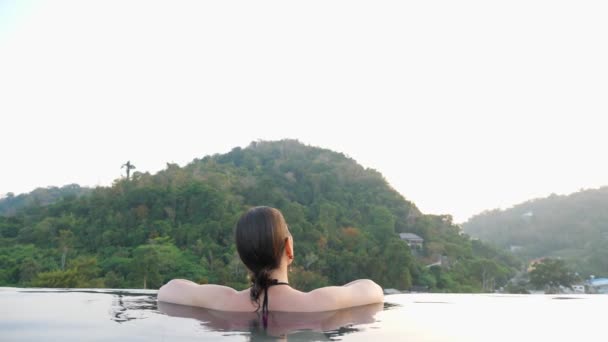 Brunette looks at green forestry hills sitting in pool water — Stock Video