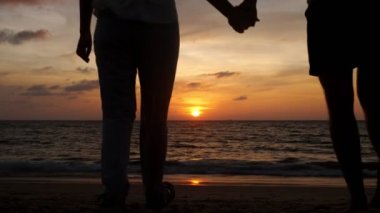 İnsanlar gün batımında sahilden okyanusa yürüyen siluetler.