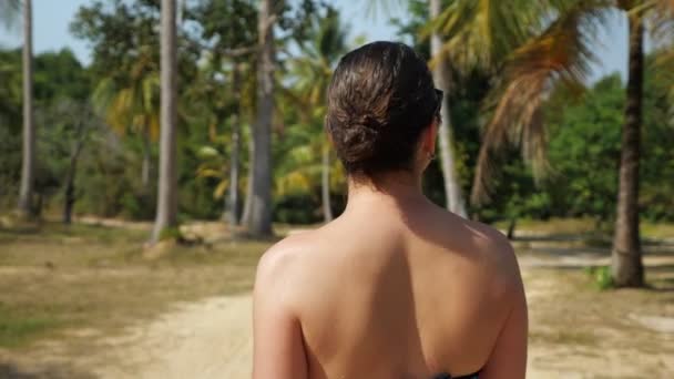 Chica camina por la arboleda y se vuelve contra las palmeras — Vídeos de Stock