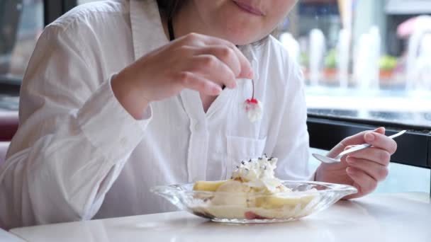Молодая женщина в белой рубашке ест вишню с мороженым — стоковое видео