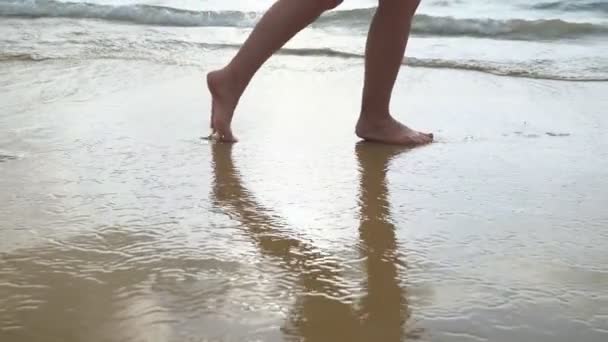 Pies femeninos caminando sobre arena dorada en la playa con olas del océano en el fondo . — Vídeos de Stock