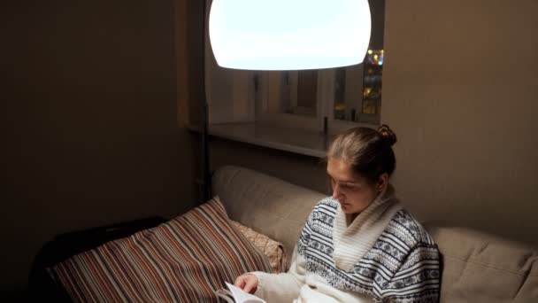 Βραδινή διασκέδαση. Μια γυναίκα διαβάζει ένα βιβλίο στον καναπέ. — Αρχείο Βίντεο