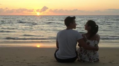 Okyanus sahilinde oturan sevimli, genç çift kucaklaşmaları ve öpücükleri.