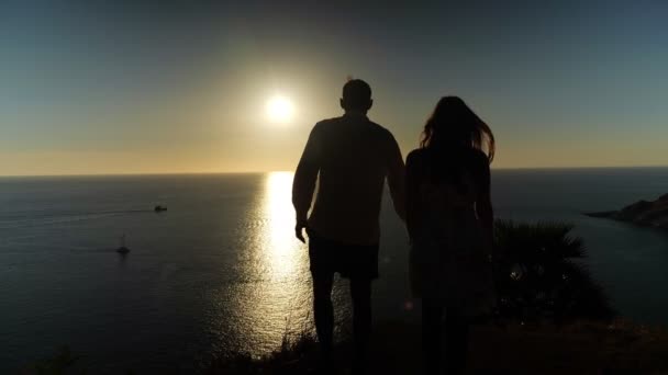 Par de siluetas de pie en el borde de la playa admirando puesta de sol — Vídeos de Stock