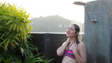 Renkli bikinili kız otelin açık hava duşunun altında ürperiyor.