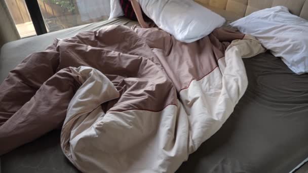 Young girl in shirt covers large bed with brown blanket and fixes near white pillows — Stock Video