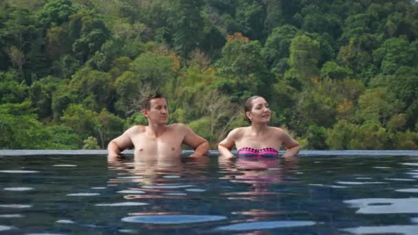 Pareja alegre sonríe y se relaja en el agua de la piscina azul grande — Vídeo de stock