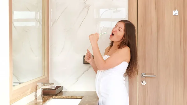 Hübsche Dame putzt Zähne und singt in weiße Zahnbürste — Stockfoto