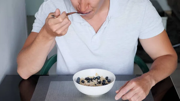 Recognizable guy in white t-shirt eats delicious porridge cereals — Stock Photo, Image