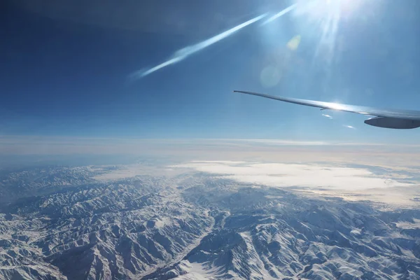 Odległe pasmo górskie przeciwko błękitnemu niebu z okna samolotu — Zdjęcie stockowe