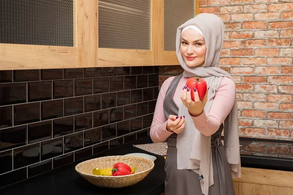 Ama de casa en hijab sostiene y muestra pimienta en la mano en la cocina — Foto de Stock