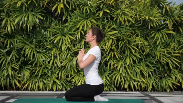 Young woman meditates on a background of green foliage outdoors — Stock Video