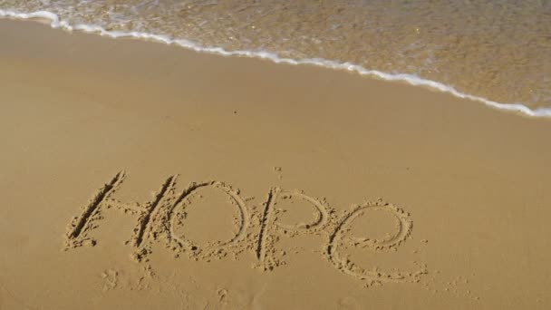 Inscriptie in het zand. De zeegolf spoelt het woord hoop weg. — Stockvideo