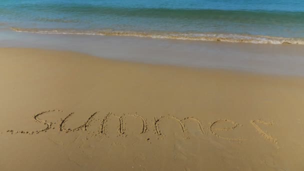 Felirat a homokba. A tengeri hullám közeledik a nyár szóhoz. — Stock videók