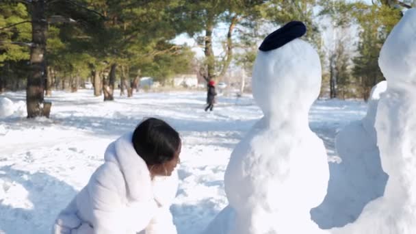 Menina bonita com pele escura em casaco de pele e luvas pretas faz boneco de neve — Vídeo de Stock