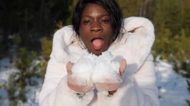 Dark-skinned girl blows on snow sparkling under sun rays — Stock Video