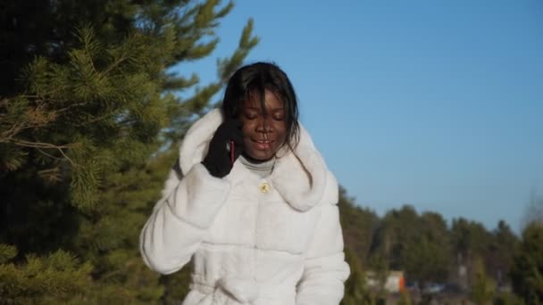 Chica con piel negra camina por el bosque y habla por teléfono — Vídeo de stock