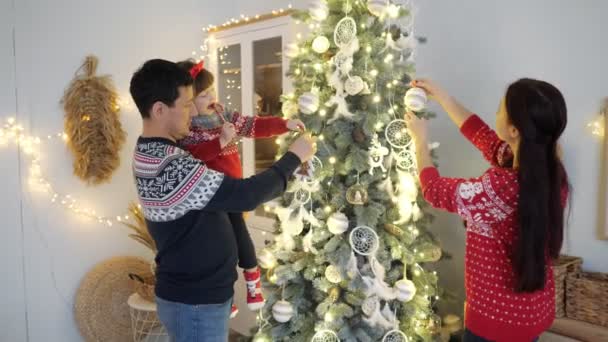 Ailesi kızıyla birlikte aydınlanmış Noel ağacını süslüyor. — Stok video