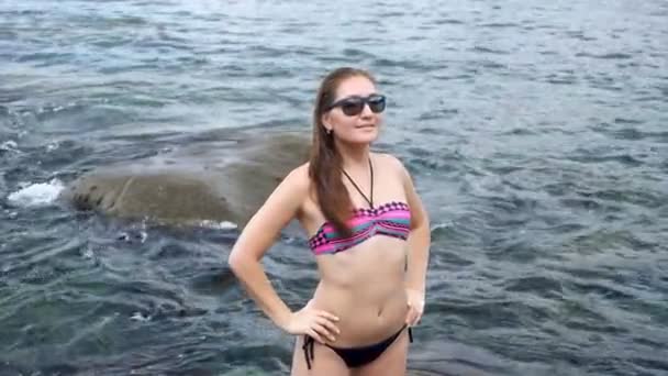 Lady poses standing against boundless ocean washing rocks — стоковое видео