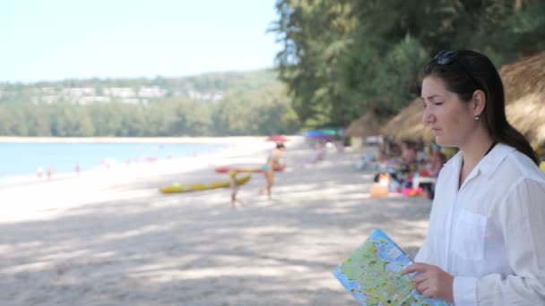 Dame komt naar oceaan strand holding map en volgt aanwijzingen — Stockvideo