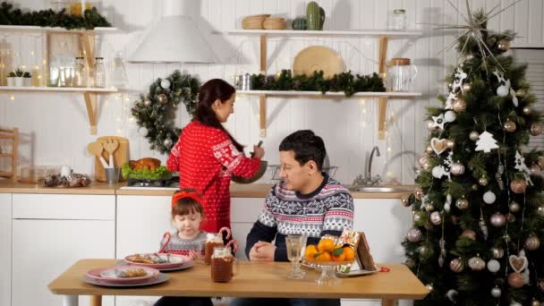 Madre cocina cena festiva y padre se sienta con niña niño — Vídeo de stock