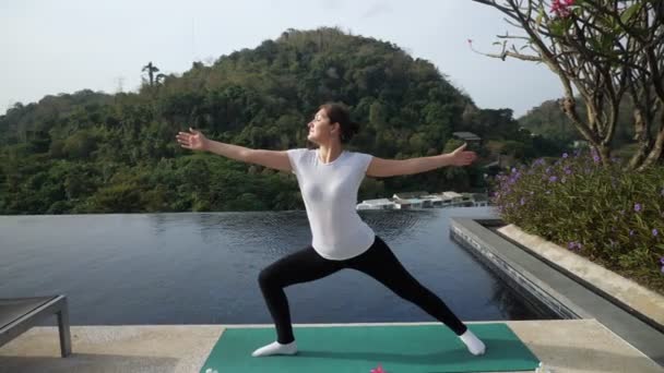 Yoga al aire libre. Mujer en una pose de guerrero cerca de la piscina — Vídeo de stock