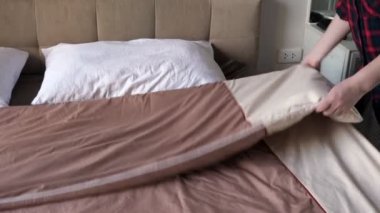 Gömlekli kadın otel odasında kahverengi battaniyeyle yatağı örtüyor.